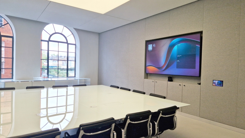 Large 16 person meeting room Large 16 person meeting room filled with natural light through arched windows and ceiling light installation. There is a large display screen with video conferencing equipment.